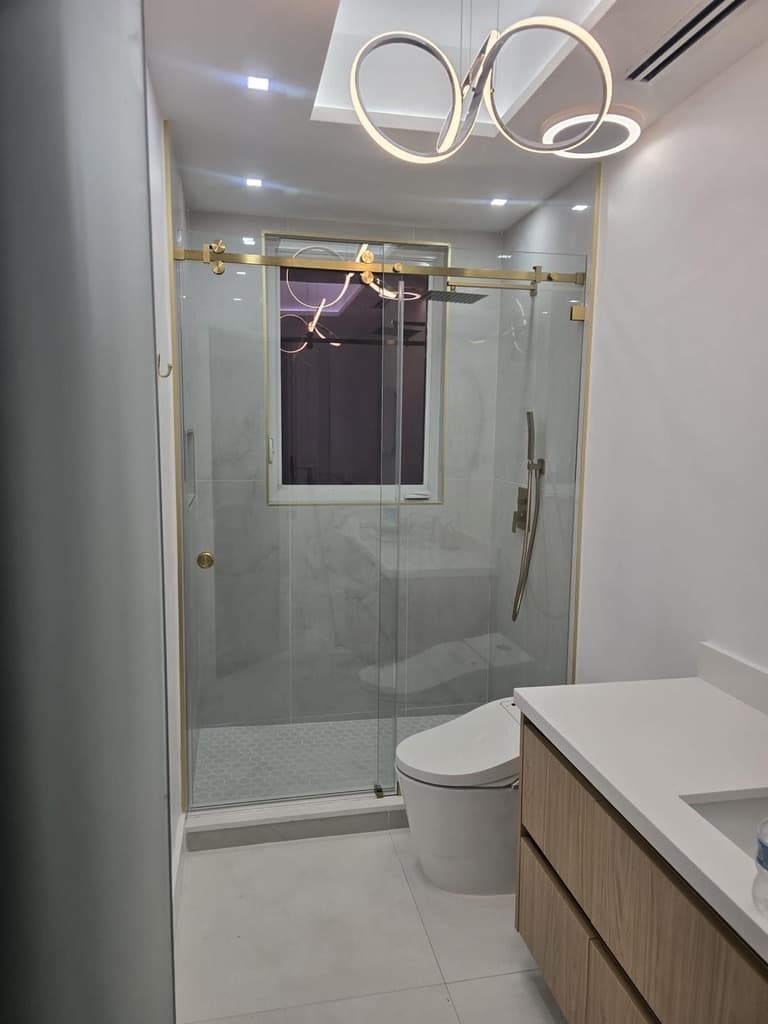 Luxury bathroom with gold fixtures, frameless glass shower, and modern chandelier